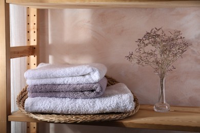 Stacked soft towels and flowers on wooden shelf indoors