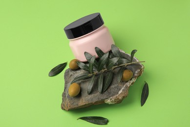 Jar of cream and olives on light green background, flat lay