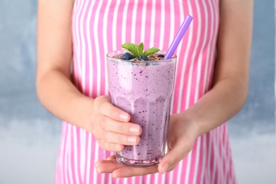 Woman holding glass of delicious blueberry smoothie on blue background, closeup