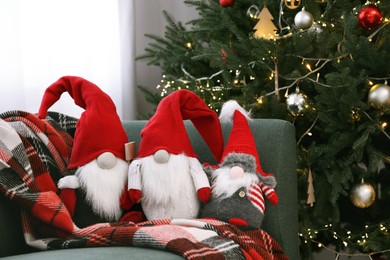 Photo of Funny decorative gnomes on sofa near Christmas tree