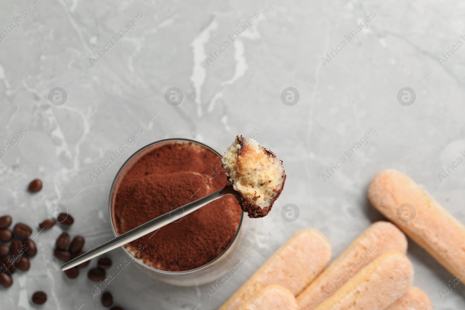 Photo of Tasty tiramisu in glass, coffee beans, spoon and biscuits on light grey table, flat lay. Space for text