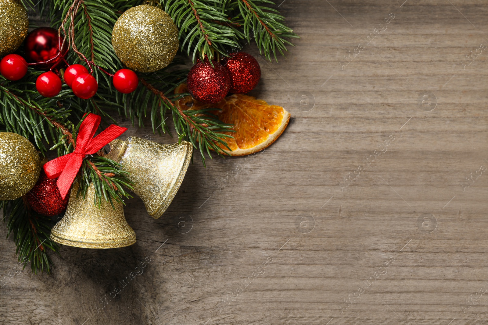 Photo of Christmas bells and fir tree branches with festive decor on wooden table, flat lay. Space for text