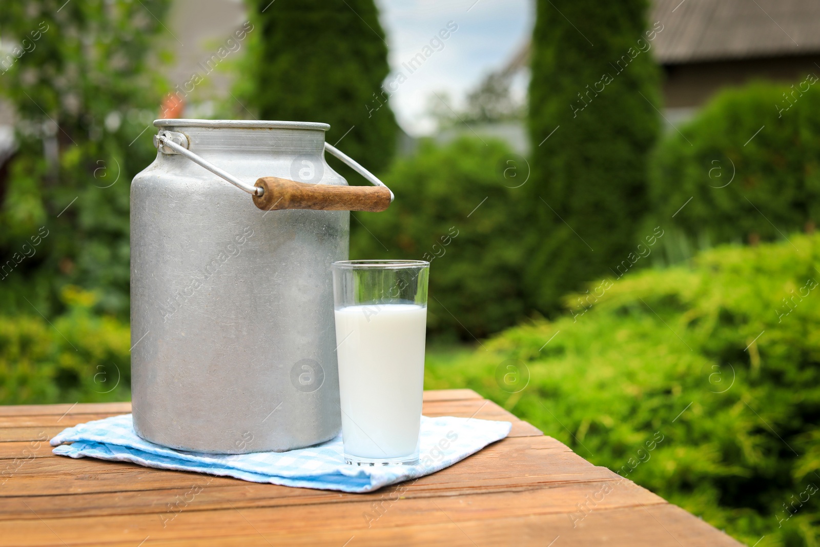 Photo of Tasty fresh milk in can and glass on wooden table outdoors, space for text