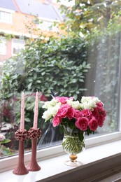 Vase with beautiful bouquet of roses and candles on windowsill indoors