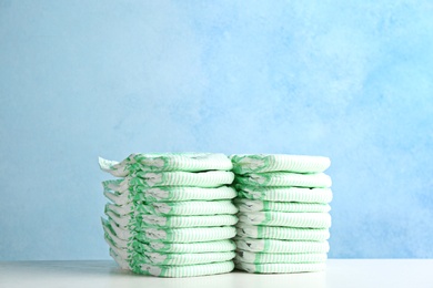 Photo of Stacks of diapers on table against color background, space for text. Baby accessories