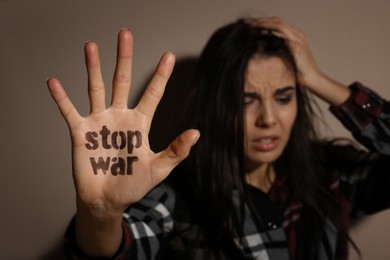 Image of Upset young woman showing palm with phrase Stop War near beige wall, focus on hand