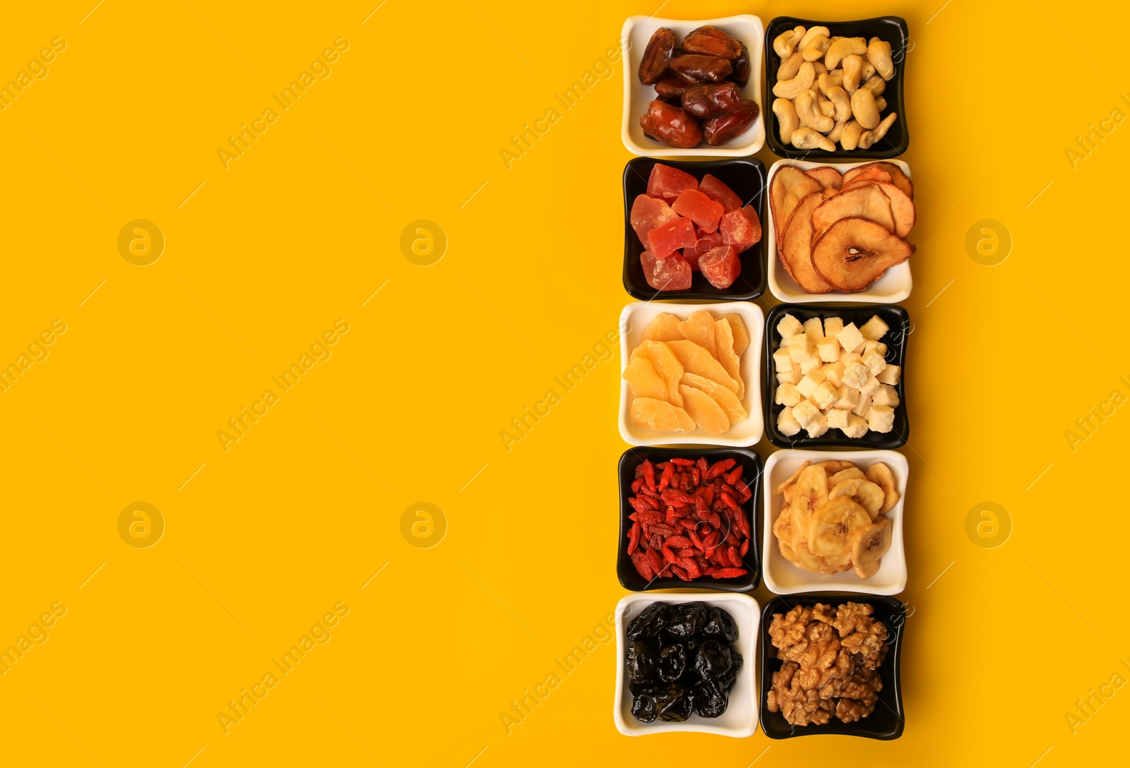 Photo of Bowls with dried fruits and nuts on yellow background, flat lay. Space for text