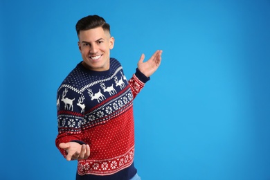 Photo of Happy man in Christmas sweater on blue background, space for text