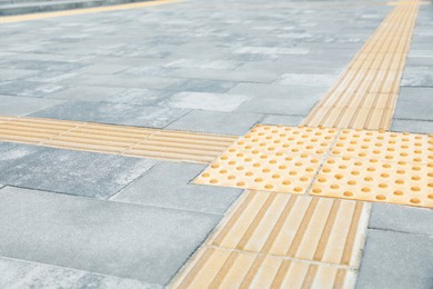 Photo of Grey pavement with tactile tiles outdoors. Public environment accessible for visually impaired