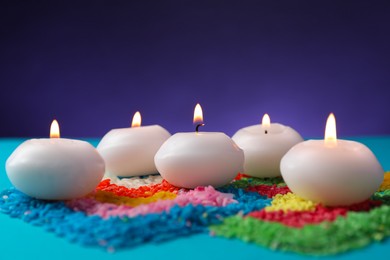 Photo of Diwali celebration. Burning candles and colorful rangoli on light blue background, closeup