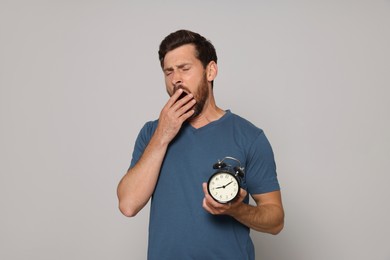 Photo of Sleepy bearded man with alarm clock on grey background