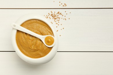 Photo of Bowl and spoon with tasty mustard sauce on white wooden table, top view. Space for text