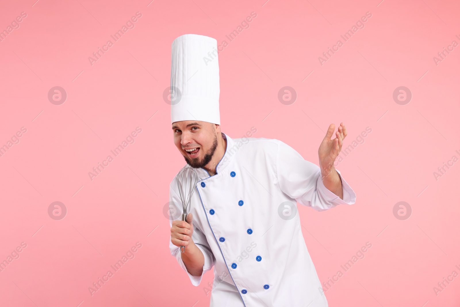 Photo of Happy professional confectioner in uniform having fun with whisk on pink background