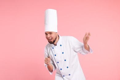 Photo of Happy professional confectioner in uniform having fun with whisk on pink background