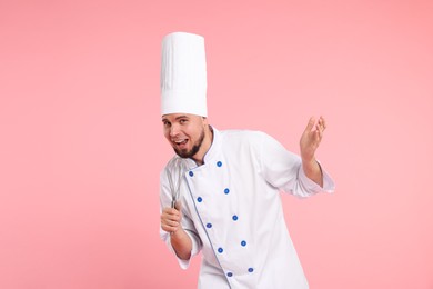 Happy professional confectioner in uniform having fun with whisk on pink background