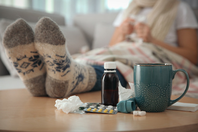 Photo of Person in warm socks near table with different remedies indoors, closeup. Influenza virus
