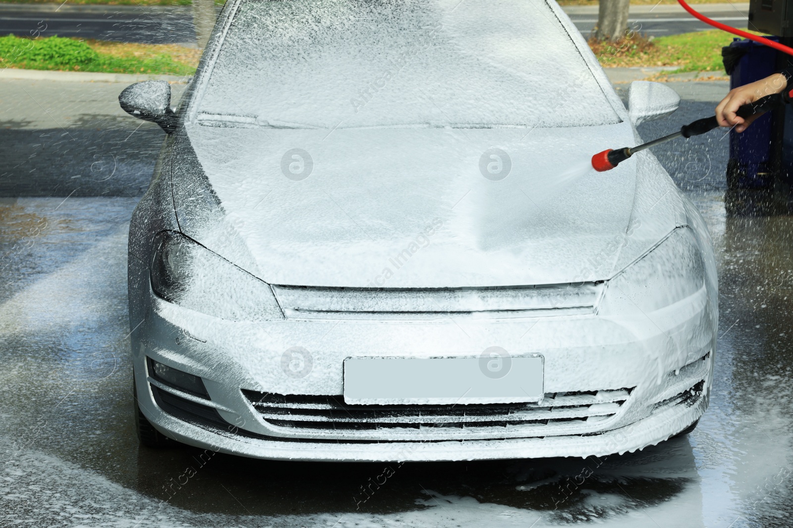 Photo of Man washing auto with high pressure water jet at outdoor car wash, closeup