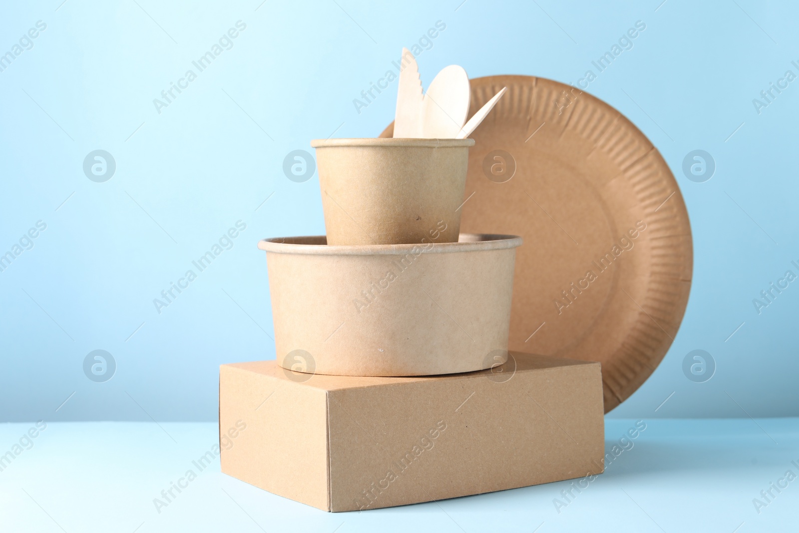 Photo of Eco friendly food packaging. Paper containers and tableware on white table against light blue background