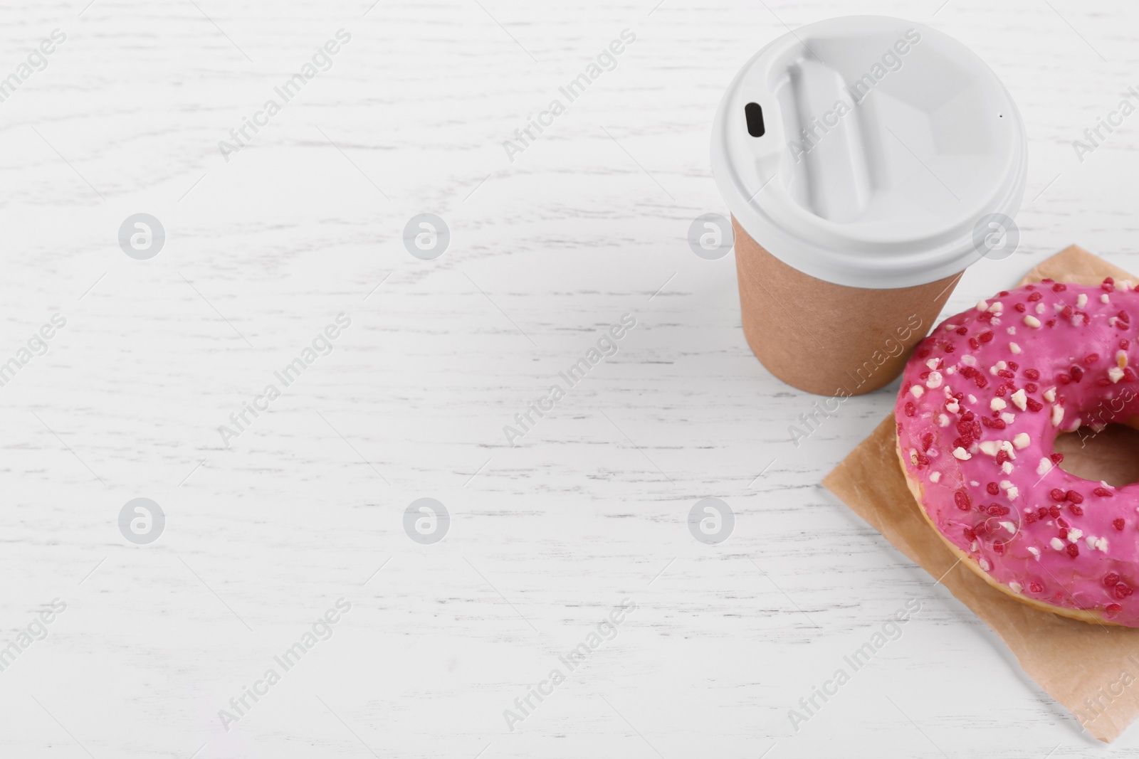 Photo of Tasty frosted donut and hot drink on white wooden table, space for text