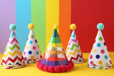 Different bright party hats with pompoms on color background