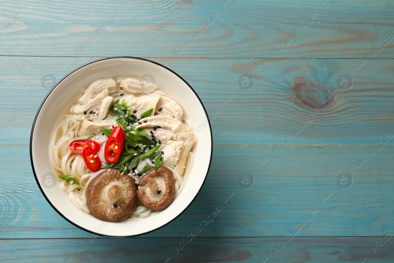 Photo of Delicious ramen with meat and mushrooms in bowl on light blue wooden table, top view. Space for text