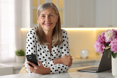 Photo of Senior woman using mobile phone at white table indoors