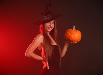 Photo of Young woman wearing witch costume with pumpkin on dark  background. Halloween party