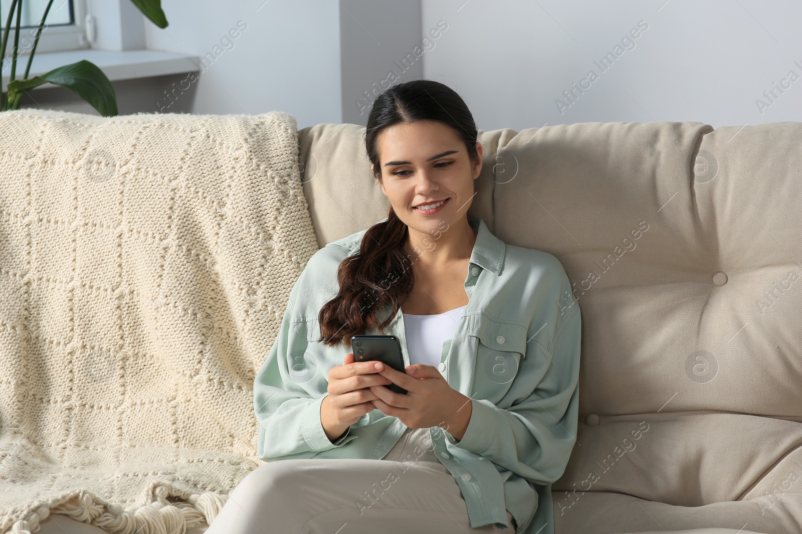 Photo of Young woman with smartphone sitting on sofa at home