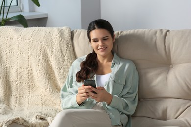 Young woman with smartphone sitting on sofa at home