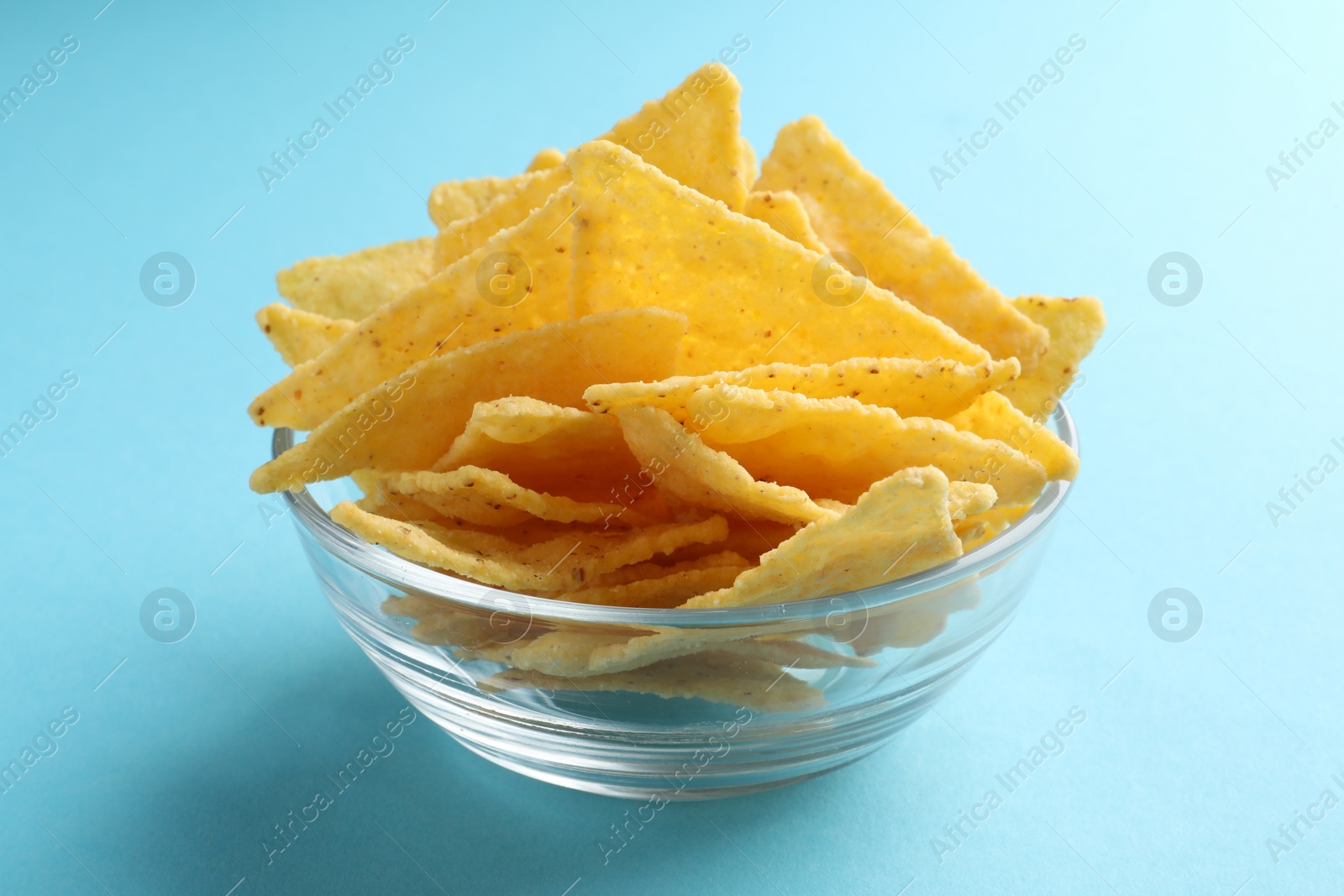 Photo of Tortilla chips (nachos) in glass bowl on light blue background, closeup