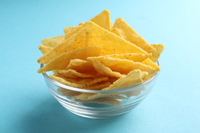 Photo of Tortilla chips (nachos) in glass bowl on light blue background, closeup