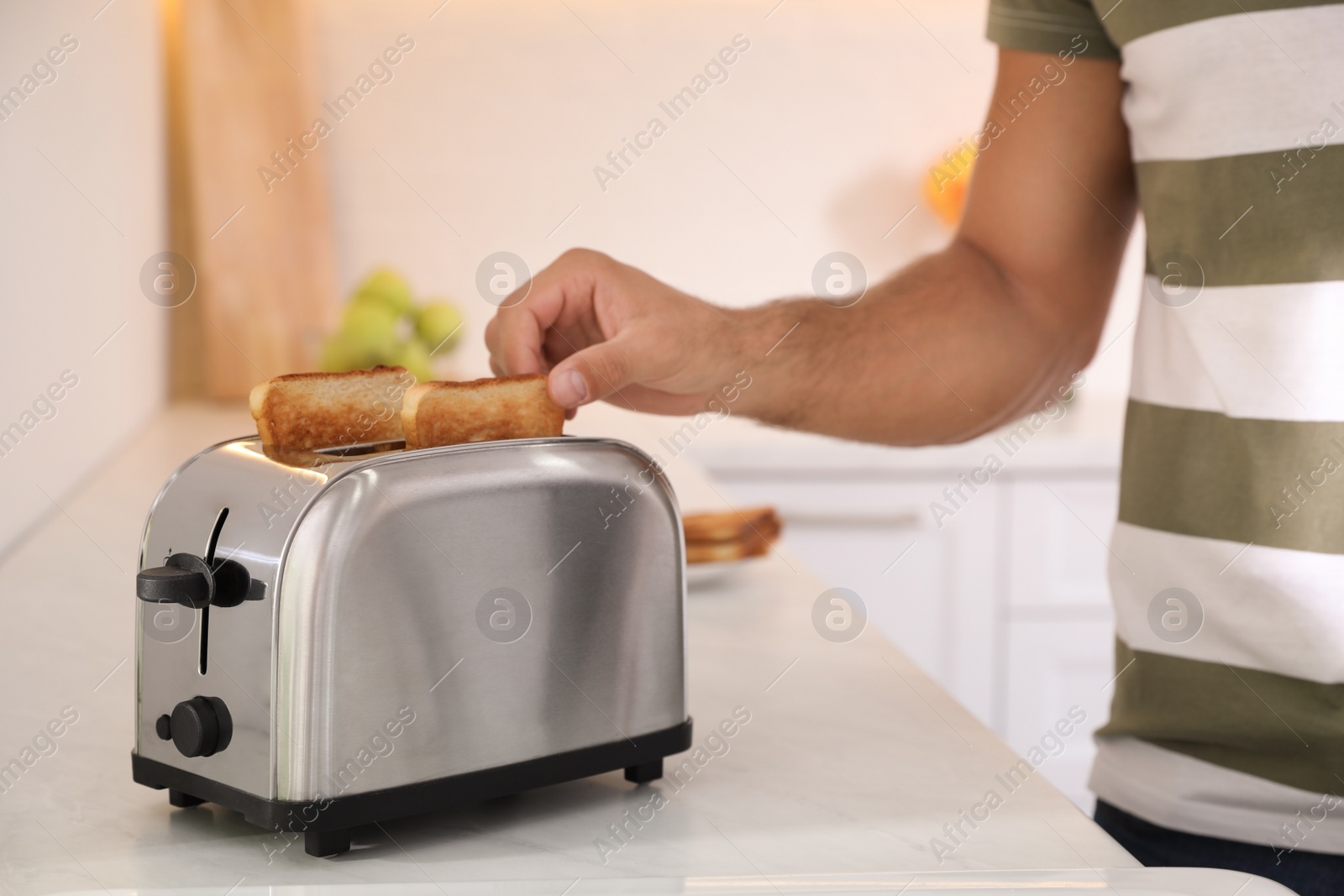 Photo of Man taking slice of bread from toaster in kitchen, closeup