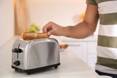 Man taking slice of bread from toaster in kitchen, closeup