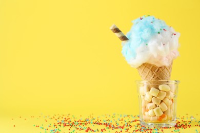 Photo of Sweet cotton candy in waffle cone on yellow background, closeup. Space for text