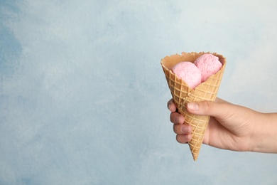 Photo of Woman holding delicious ice cream in wafer cone on light blue background, closeup. Space for text