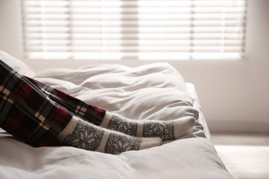 Woman wearing knitted socks on bed with soft blanket at home, closeup