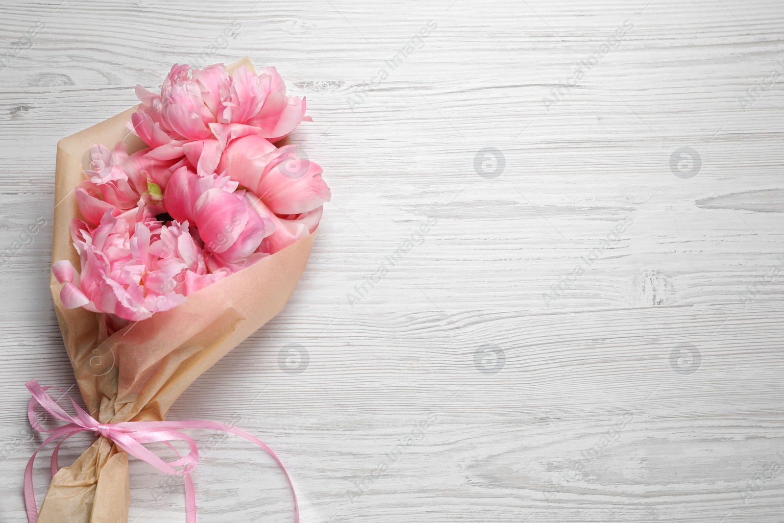 Photo of Beautiful bouquet of pink peonies wrapped in paper on white wooden table, top view. Space for text