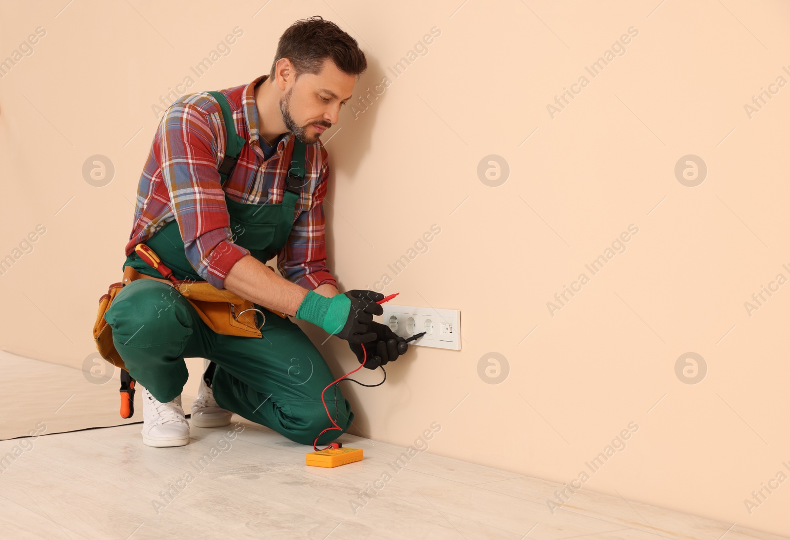 Photo of Electrician in uniform with tester checking voltage indoors. Space for text
