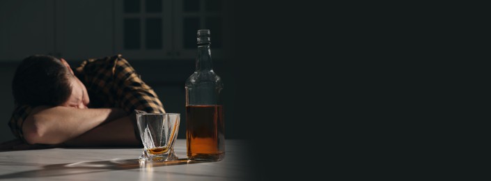 Suffering from hangover. Man with alcoholic drink on table in kitchen, selective focus. Banner design with space for text