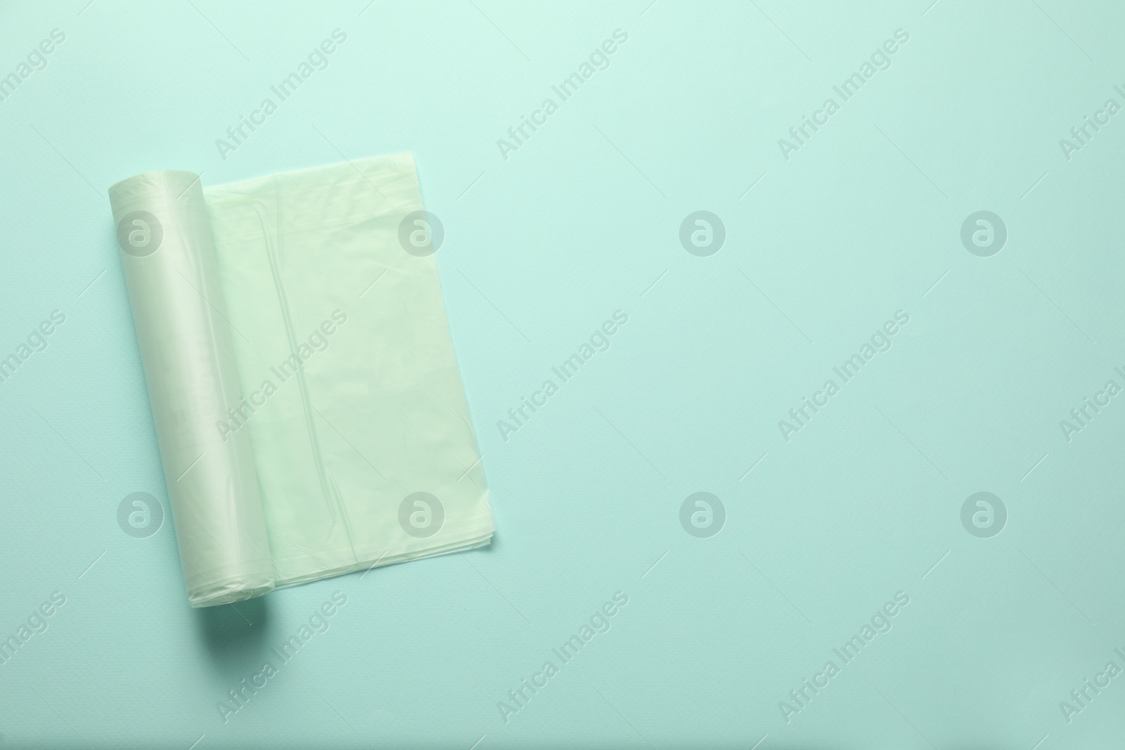 Photo of Roll of garbage bags on turquoise background, top view. Space for text