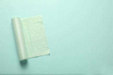 Photo of Roll of garbage bags on turquoise background, top view. Space for text