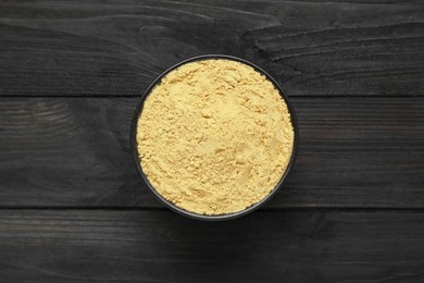 Photo of Bowl of aromatic mustard powder on black wooden table, top view