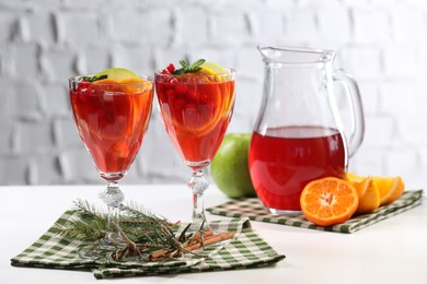 Photo of Christmas Sangria cocktail in glasses and jug, ingredients and fir tree branch on white table against brick wall