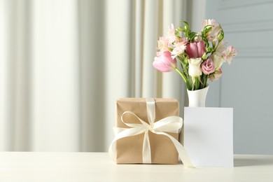 Photo of Happy Mother's Day. Gift box, blank card and bouquet of beautiful flowers in vase on white table indoors. Space for text