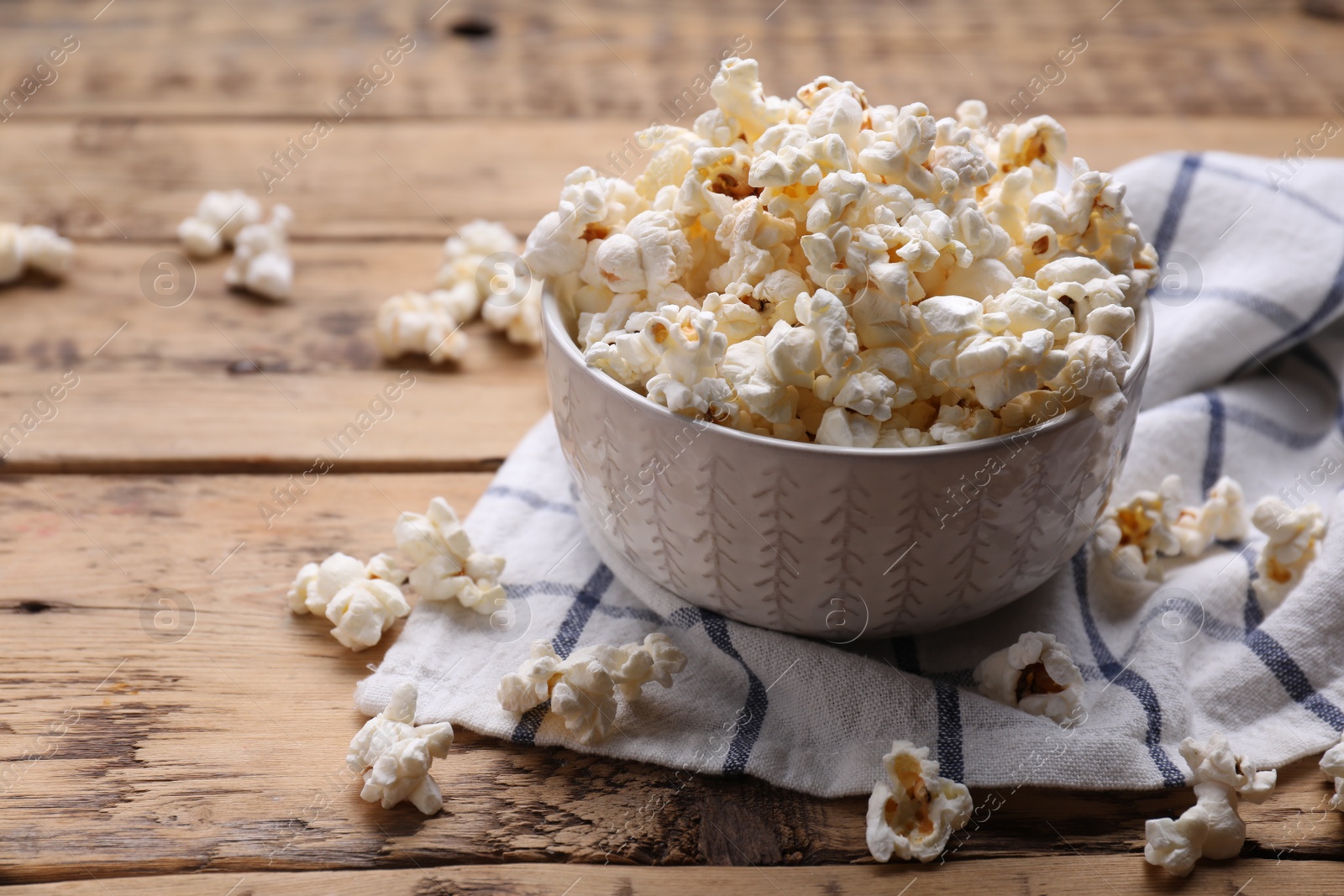 Photo of Bowl of tasty popcorn on wooden table, space for text