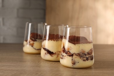 Photo of Delicious tiramisu in glasses on wooden table