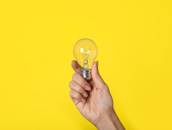 Photo of Woman holding incandescent light bulb on yellow background, closeup