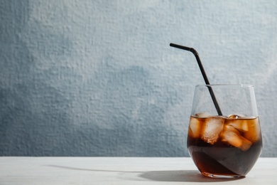 Glass of refreshing cola with ice cubes and straw on table. Space for text