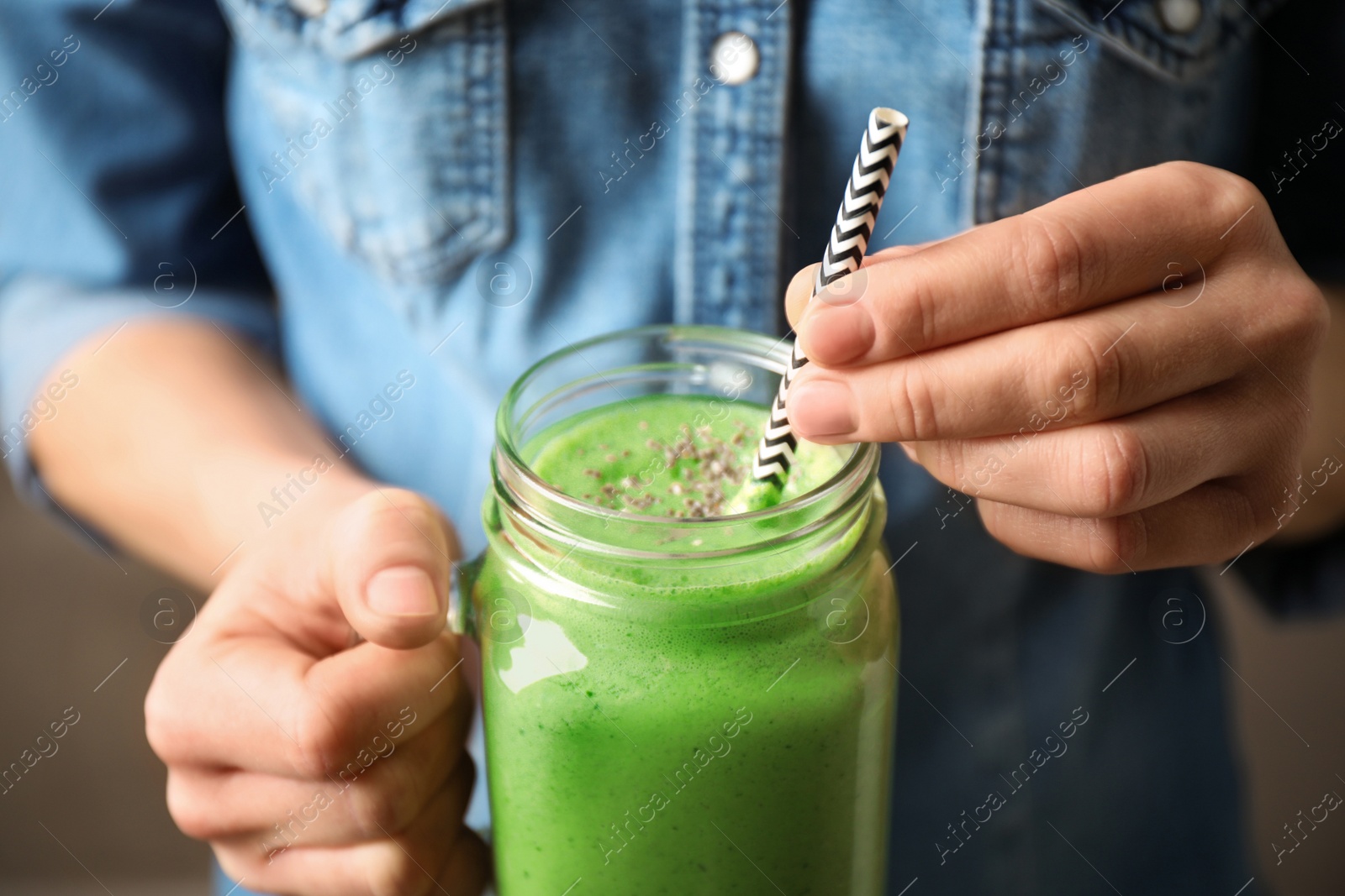 Photo of Woman holding tasty kale smoothie on brown background, closeup