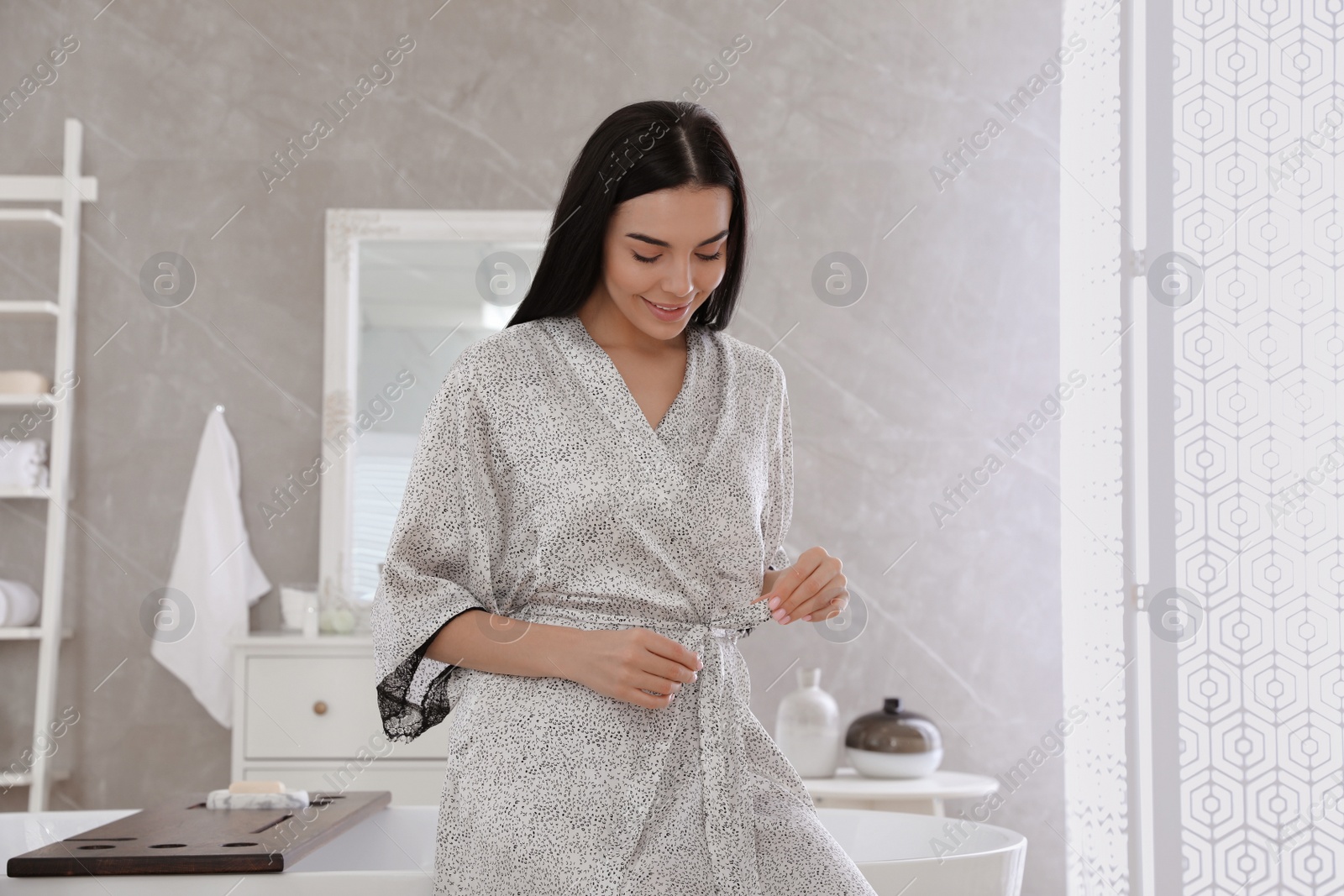 Photo of Beautiful young woman in silk robe near bathtub at home